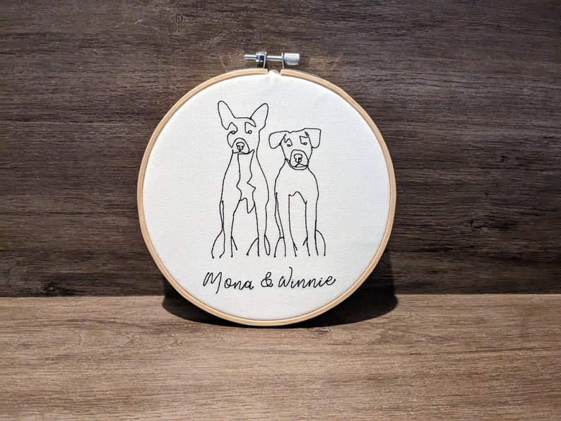 Op de afbeelding: Borduurwerk op een ronde ring met twee honden, Mona & Winnie, in een eenvoudige lijntekening stijl.
