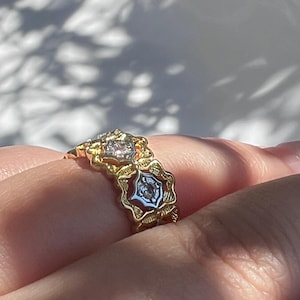 May include: A gold ring with a floral design, featuring clear gemstones. The ring has a detailed, ornate setting with a vintage aesthetic. The gemstones are set in a star-like pattern.
