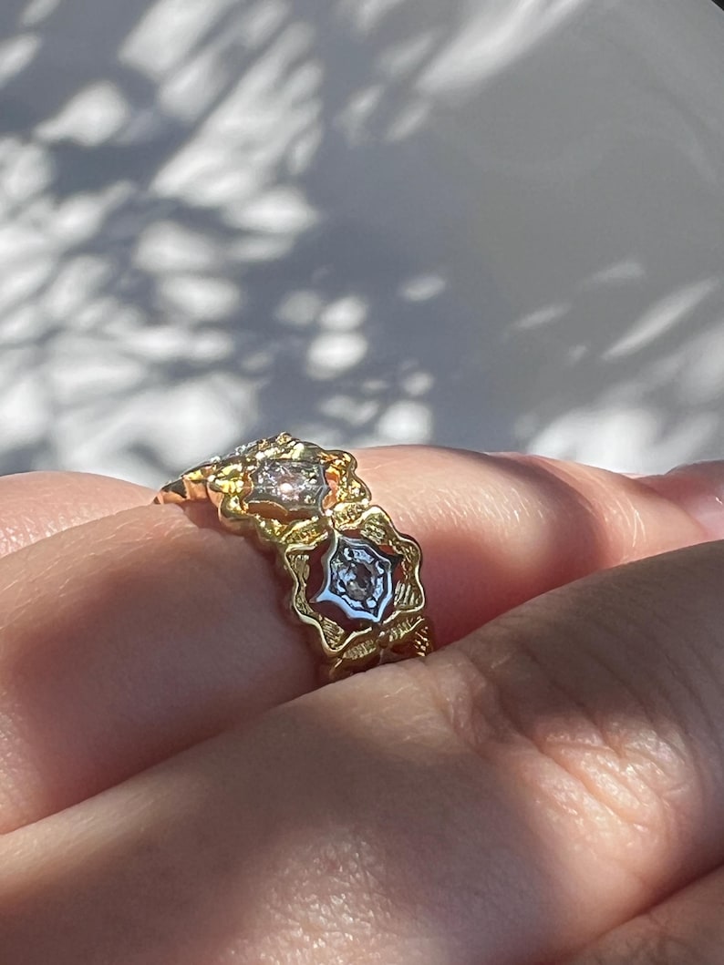 May include: A gold ring with a floral design, featuring clear gemstones. The ring has a detailed, ornate setting with a vintage aesthetic. The gemstones are set in a star-like pattern.