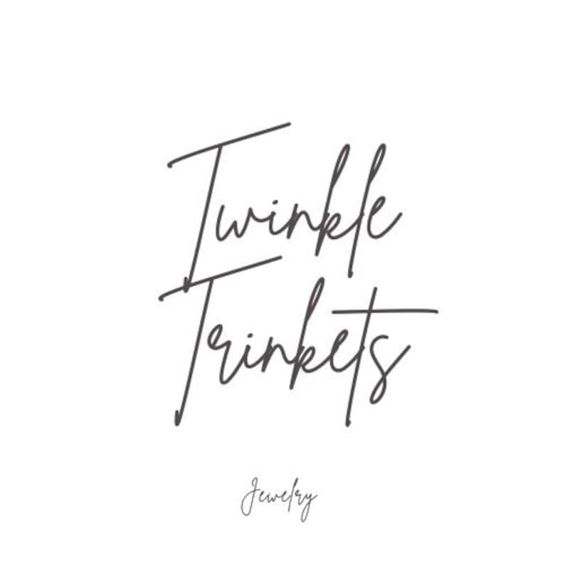 Pu&ograve; includere: Un logo su sfondo bianco con le parole "Twinkle Trinkets" in stile scritto a mano, con "Jewelry" scritto sotto in un carattere pi&ugrave; piccolo e simile.