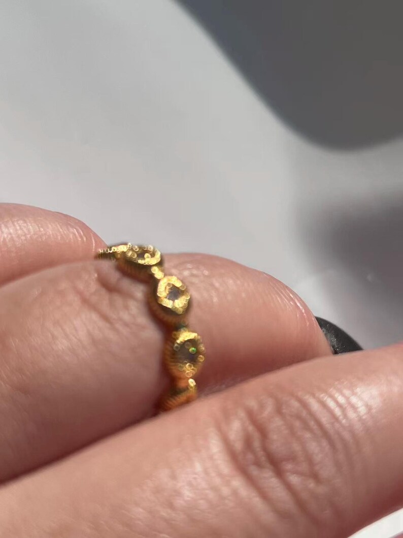 May include: A gold ring with a repeating pattern of small, textured, oval-shaped designs. Each oval has a small, clear stone in the center. The ring is worn on a finger.