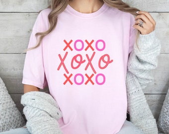 May include: A pink t-shirt with the text "XOXO" repeated three times in a pink and red neon-style font.