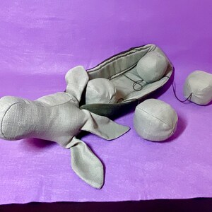 Puede incluir: Un elefante de peluche gris con un barco de tela sujeto a su espalda. El barco tiene un forro de tela gris y cuatro bolas de tela gris sujetas a &eacute;l.