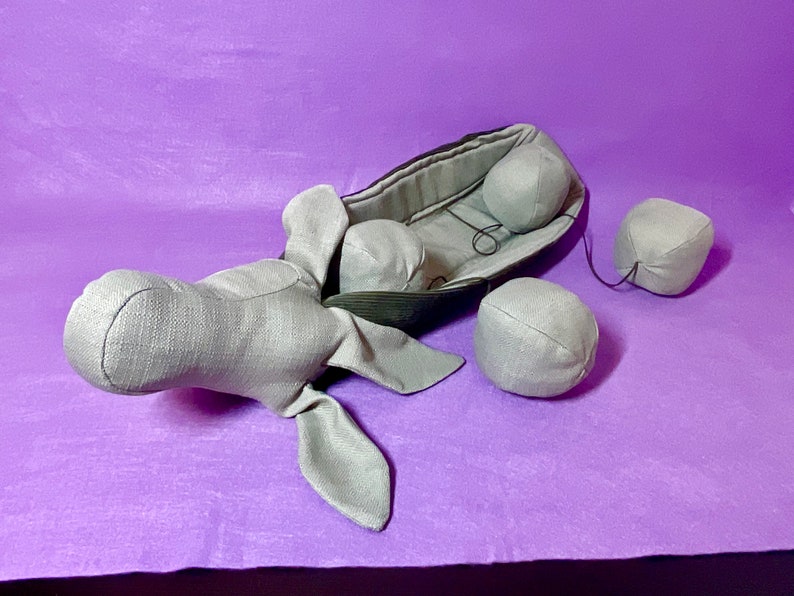 Puede incluir: Un elefante de peluche gris con un barco de tela sujeto a su espalda. El barco tiene un forro de tela gris y cuatro bolas de tela gris sujetas a &eacute;l.