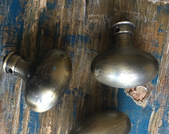 May include: Three antique oval-shaped door knobs with a brushed brass finish. The knobs are on a weathered wooden surface.