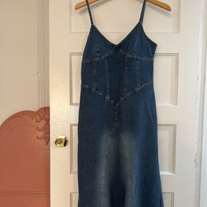 May include: A long, blue denim dress with a fitted bodice and a flowing skirt. The dress has a V-neckline and thin spaghetti straps.