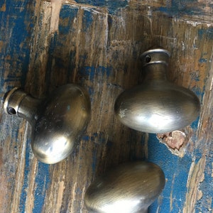 Könnte beinhalten: Drei antike, ovale Türknauf mit gebürstetem Messing-Finish. Die Knäufe befinden sich auf einer verwitterten Holzoberfläche.