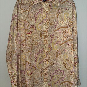 May include: A long-sleeved button-down shirt with a paisley pattern in shades of beige, yellow, pink, and brown. The shirt has a classic collar and buttoned cuffs. The Tommy Hilfiger logo is visible on the collar.