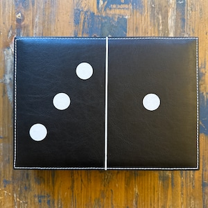 May include: A black leather domino with white dots. The domino has three dots on one side and one dot on the other side.