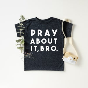 Puede incluir: Una camiseta de manga corta gris oscuro con el texto "PRAY ABOUT IT, BRO." impreso en blanco.