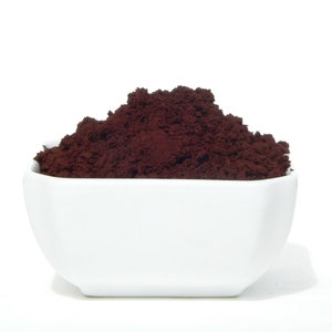 May include: A white ceramic bowl filled with a generous amount of dark brown cocoa powder.