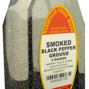 May include: A clear glass jar filled with black peppercorns. The jar has a red lid and a yellow label that reads "Marshalls Creek Spices" and "Smoked Black Pepper Ground 6 Ounces".