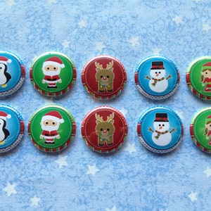 May include: Ten circular pinback buttons arranged in two rows of five. The designs feature Christmas characters including a penguin, Santa Claus, a reindeer, a snowman, and an elf, each set against a colorful background with a decorative border.