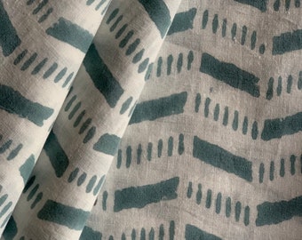 May include: A white fabric with a teal blue geometric pattern of horizontal lines and dashes. The fabric is folded in half, showing the pattern on both sides.