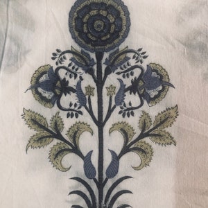 Puede incluir: Una tela blanca con un estampado floral azul y verde. El estampado presenta una gran flor central rodeada de flores y hojas más pequeñas.