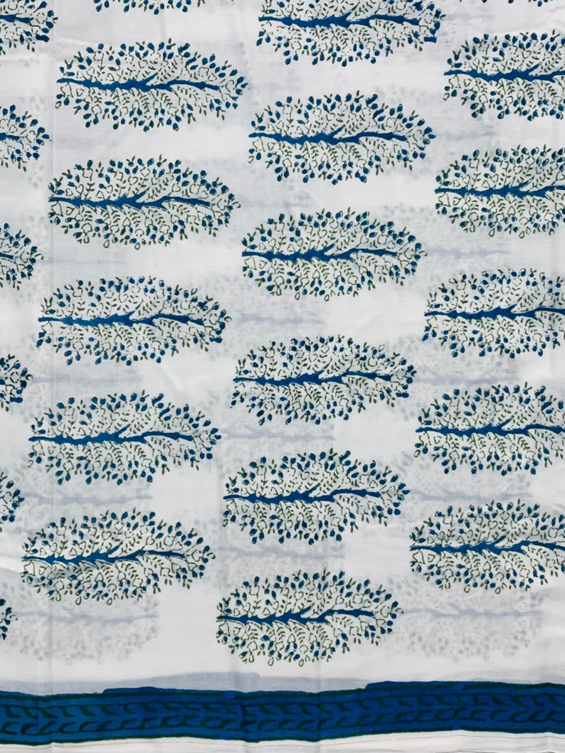 May include: White fabric with a repeating pattern of blue and green stylized tree branches. The fabric has a blue and green border.