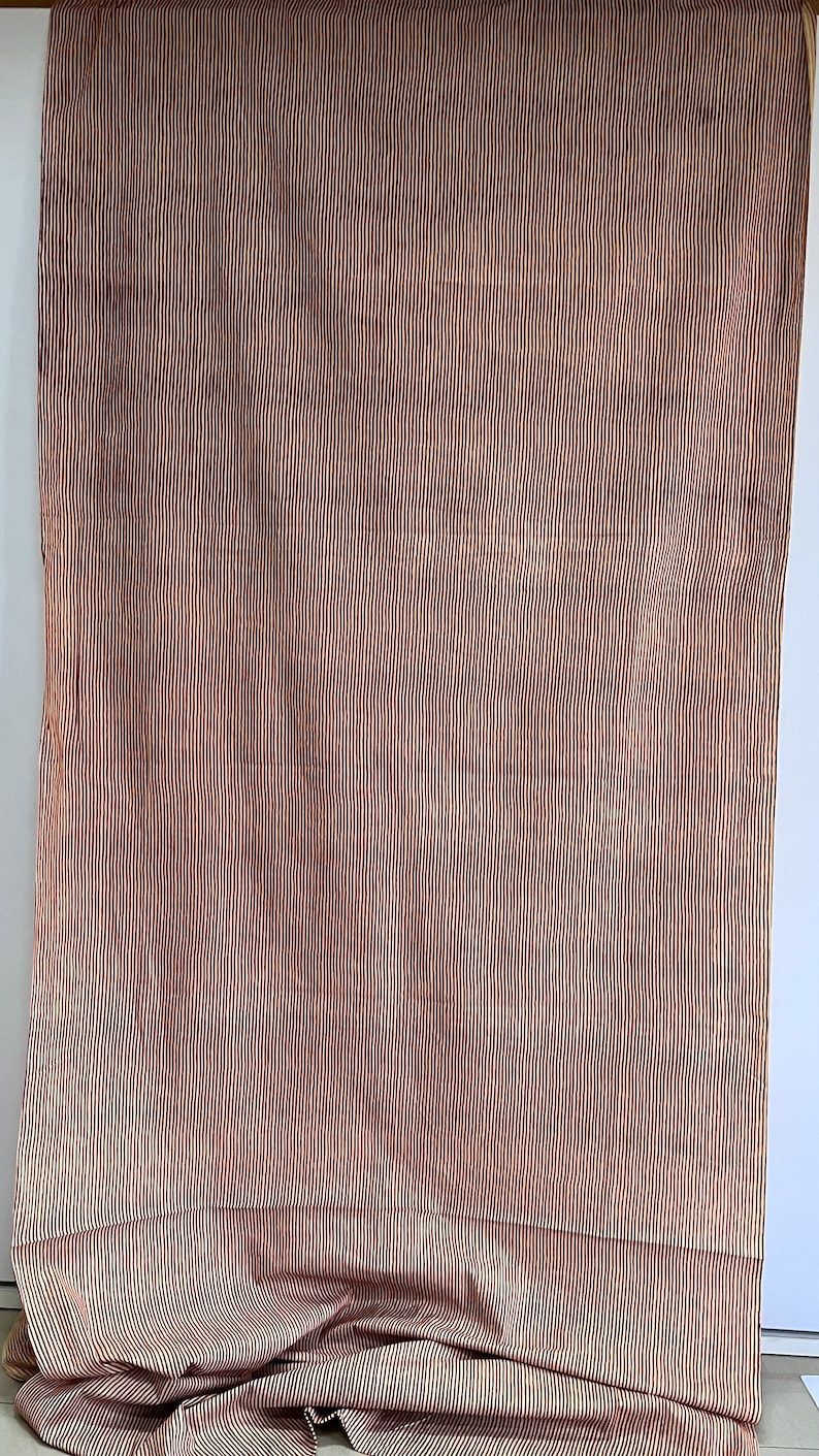 May include: A fabric with a vertical striped pattern in shades of brown and cream. The fabric is draped, with the bottom portion folded and gathered, revealing the pattern's continuity.