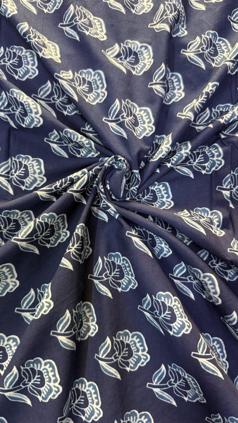 May include: Blue cotton fabric with a white floral pattern. The fabric is folded and shows the pattern repeating.