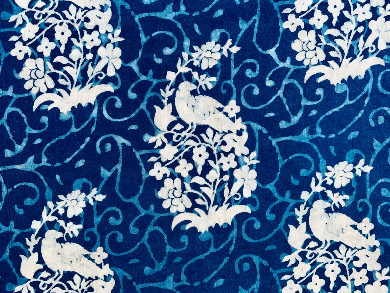 May include: A blue and white fabric with a repeating pattern of birds and flowers. The birds are white and the flowers are white with blue centers. The background is a deep blue.