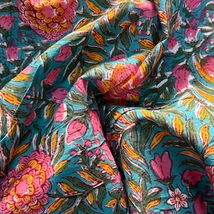 Könnte beinhalten: Nahaufnahme eines Stoffes mit floralem Muster. Der Stoff zeigt große rosa und orangefarbene Blumen, grüne Blätter und kleine weiße Blüten auf türkisfarbenem Hintergrund. Der Stoff ist gefaltet und erzeugt Schatten und Tiefe.