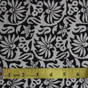 May include: Black and white fabric with a floral pattern. A yellow tape measure is placed on the fabric, showing measurements in inches.