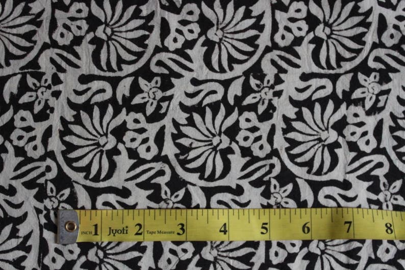 May include: Black and white fabric with a floral pattern. A yellow tape measure is placed on the fabric, showing measurements in inches.