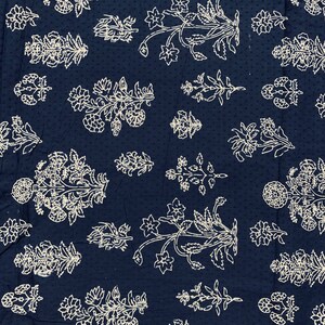 May include: A dark blue fabric with a white floral pattern. The fabric is covered in small white dots and features a repeating design of stylised flowers and leaves.