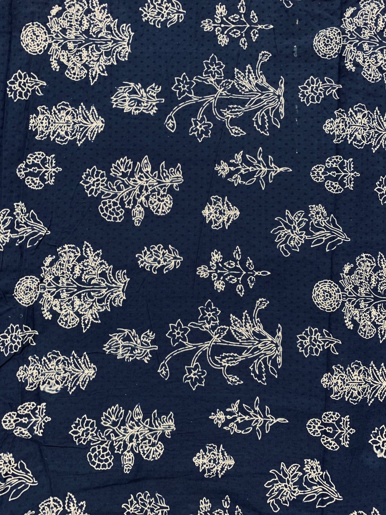 May include: A dark blue fabric with a white floral pattern. The fabric is covered in small white dots and features a repeating design of stylised flowers and leaves.
