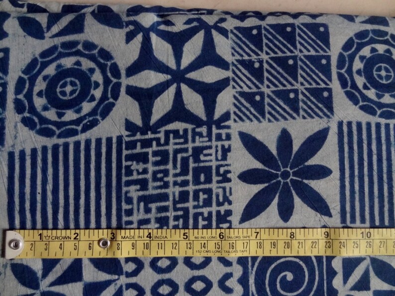 May include: A close-up of a blue and white fabric with a variety of geometric patterns. The fabric is measured with a tape measure that reads "MADE IN INDIA".