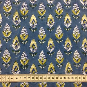 May include: Blue fabric with a repeating pattern of yellow, white, and green stylized flowers. A ruler is placed at the bottom of the image, showing measurements in inches.