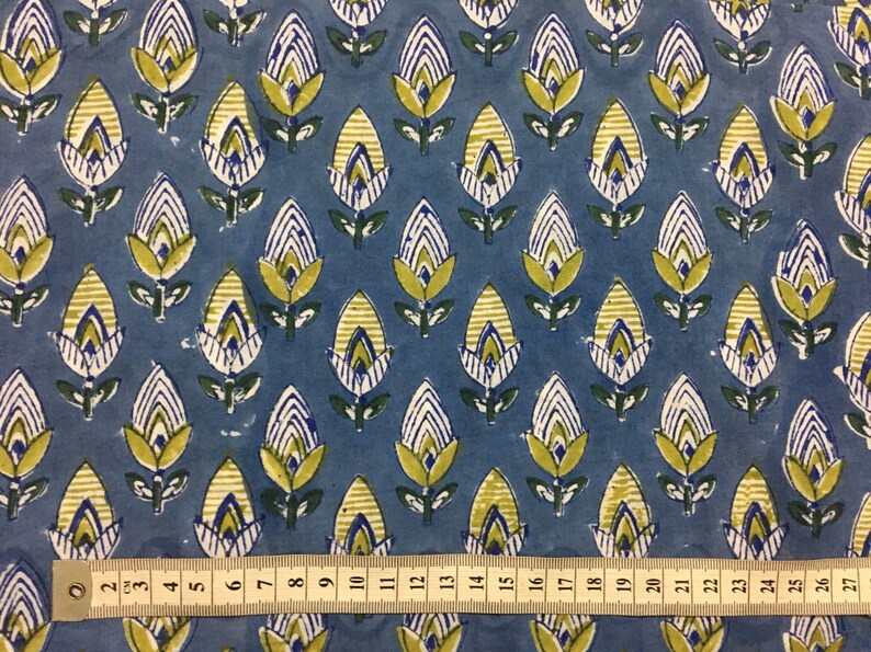 May include: Blue fabric with a repeating pattern of yellow, white, and green stylized flowers. A ruler is placed at the bottom of the image, showing measurements in inches.