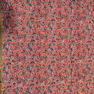 May include: A coral pink fabric with a floral pattern in shades of blue, pink, and white. The fabric is a repeating pattern of small flowers and leaves.