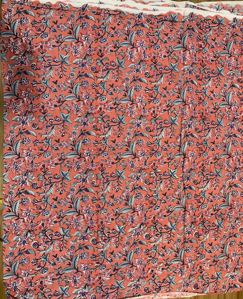 May include: A coral pink fabric with a floral pattern in shades of blue, pink, and white. The fabric is a repeating pattern of small flowers and leaves.
