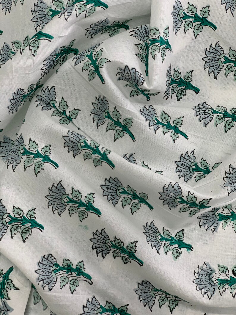 May include: White fabric with a repeating pattern of green and grey floral sprigs. The fabric is folded and has a soft, textured appearance.