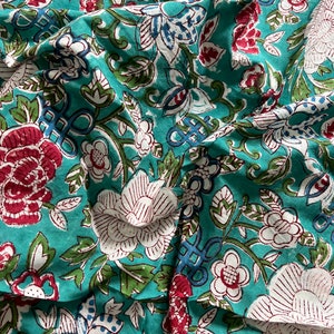 May include: Teal fabric with a white and red floral print. The fabric is folded and has a wrinkled texture.