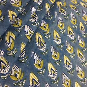 May include: Blue fabric with a repeating pattern of yellow and white stylized flowers. The flowers have a striped design and are outlined in white.