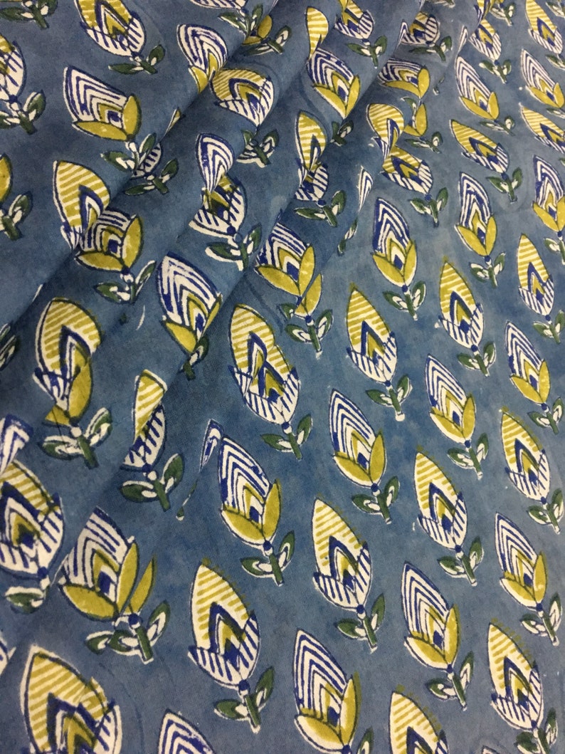 May include: Blue fabric with a repeating pattern of yellow and white stylized flowers. The flowers have a striped design and are outlined in white.