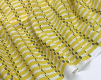 May include: A piece of fabric featuring a repeating pattern of bright yellow wavy horizontal stripes interspersed with vertical rows of small, dark green teardrop-shaped dots on a white background, displayed with soft, natural folds.