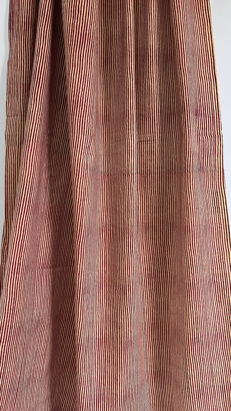May include: Close-up of a fabric with vertical stripes. The stripes alternate between a light beige and a deep burgundy color. The fabric is draped, creating soft folds and shadows.