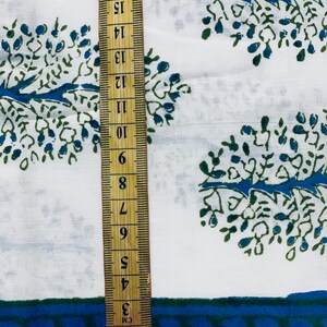 May include: White fabric with a blue and green tree pattern. A ruler is placed on the fabric, showing measurements in inches.
