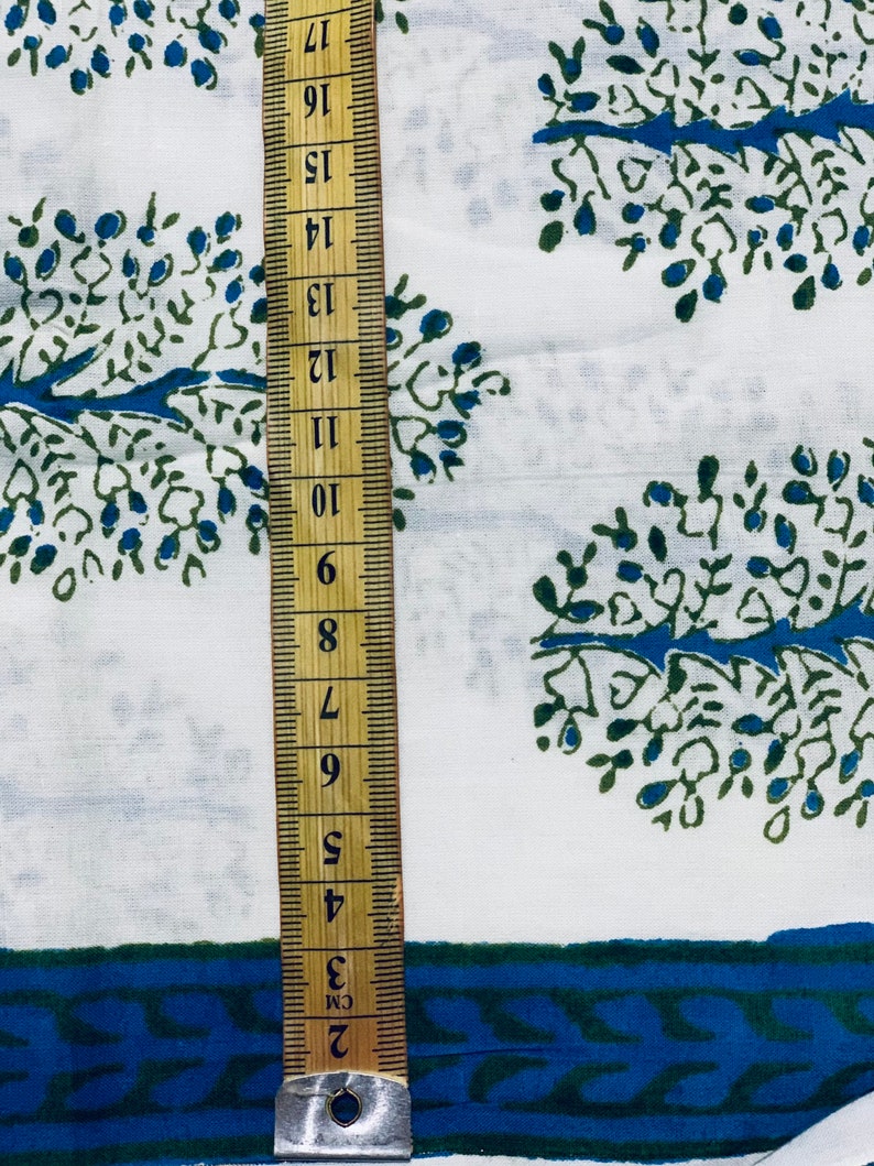 May include: White fabric with a blue and green tree pattern. A ruler is placed on the fabric, showing measurements in inches.