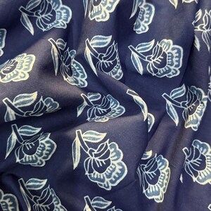 May include: A close-up of a navy blue fabric with a white floral pattern. The fabric is soft and has a subtle sheen.