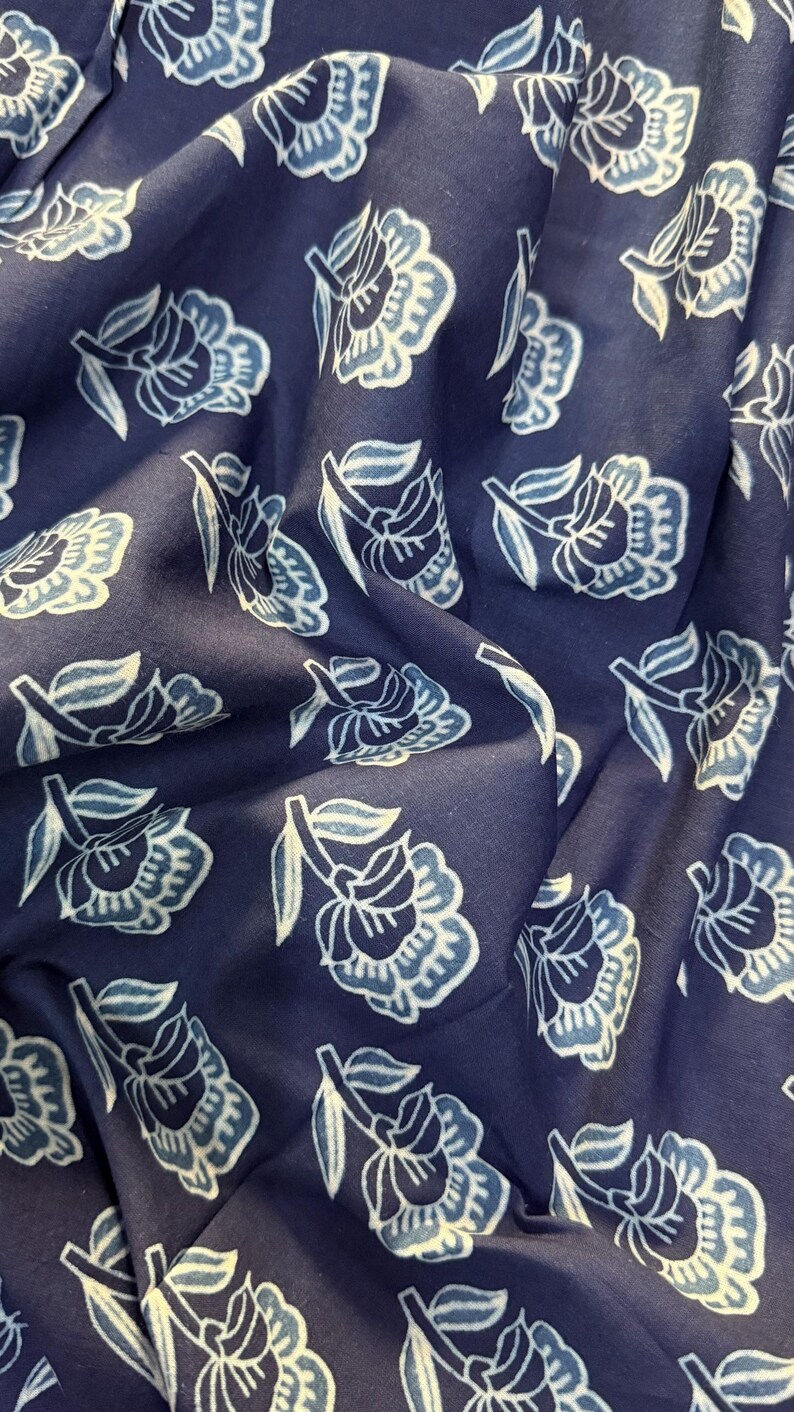 May include: A close-up of a navy blue fabric with a white floral pattern. The fabric is soft and has a subtle sheen.