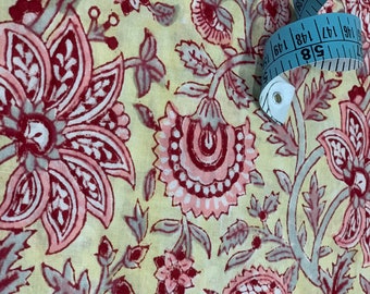 May include: A yellow fabric with a floral print in shades of pink and red. The fabric is decorated with a blue measuring tape.