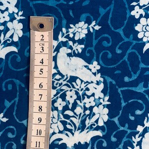 May include: A close-up of a blue fabric with a white floral and bird pattern. A ruler is placed next to the fabric, showing measurements in centimeters.