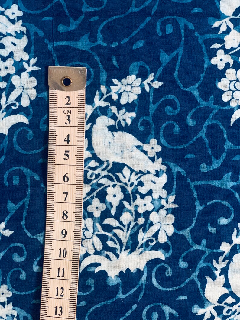 May include: A close-up of a blue fabric with a white floral and bird pattern. A ruler is placed next to the fabric, showing measurements in centimeters.