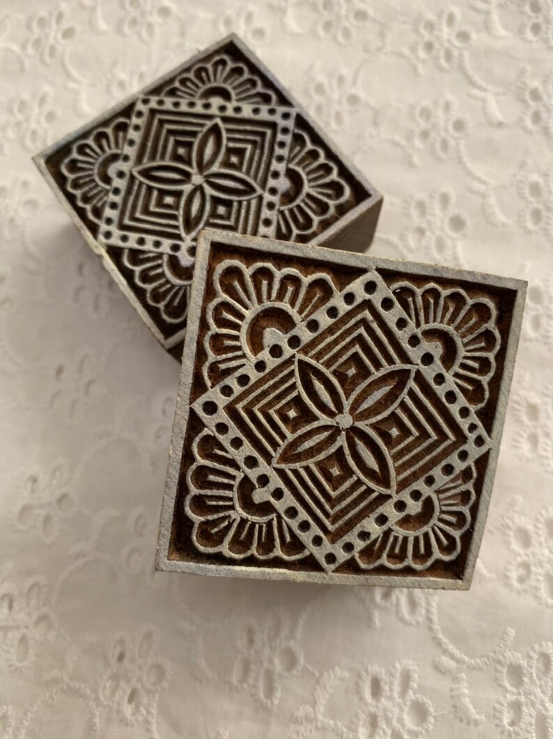 May include: Two square wooden printing blocks with intricate floral and geometric designs. The blocks are brown with a detailed pattern carved into the surface. The blocks are likely used for textile printing or decorative purposes.