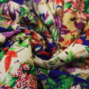 May include: A close-up of a white fabric with a colourful floral print. The fabric features a variety of flowers, including red, pink, purple, and blue flowers. The fabric is folded in a way that creates a swirl pattern.