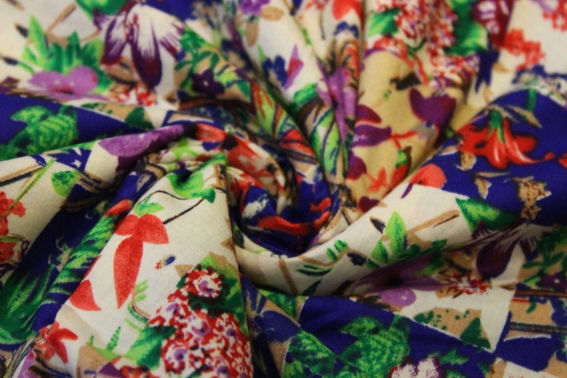 May include: A close-up of a white fabric with a colourful floral print. The fabric features a variety of flowers, including red, pink, purple, and blue flowers. The fabric is folded in a way that creates a swirl pattern.