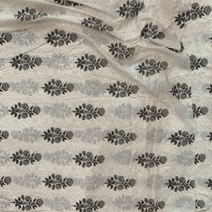 May include: White fabric with a repeating pattern of black floral sprigs. The fabric is folded and wrinkled.